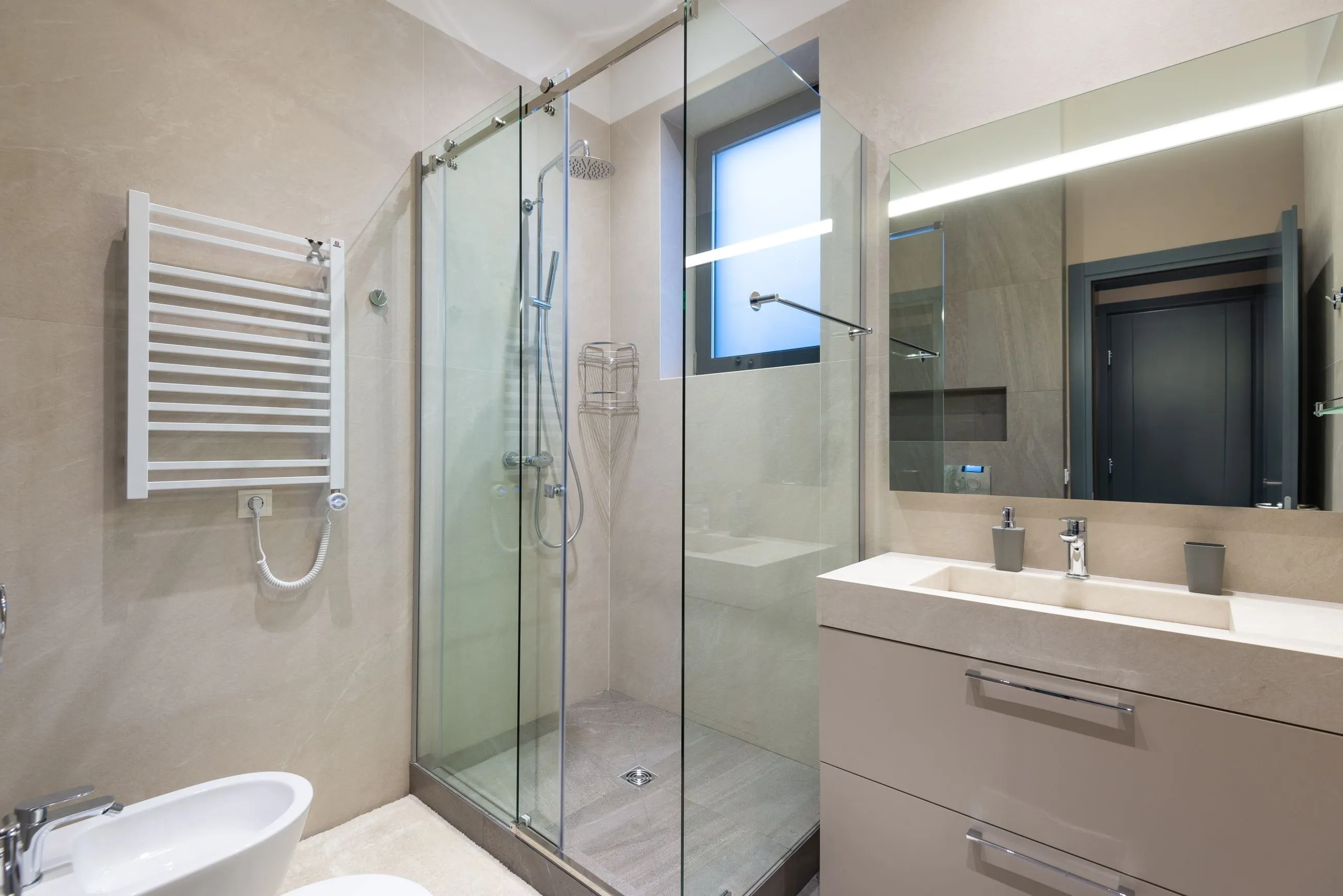 Baño en tonos piedra con ducha de mampara corredera y mueble lacado