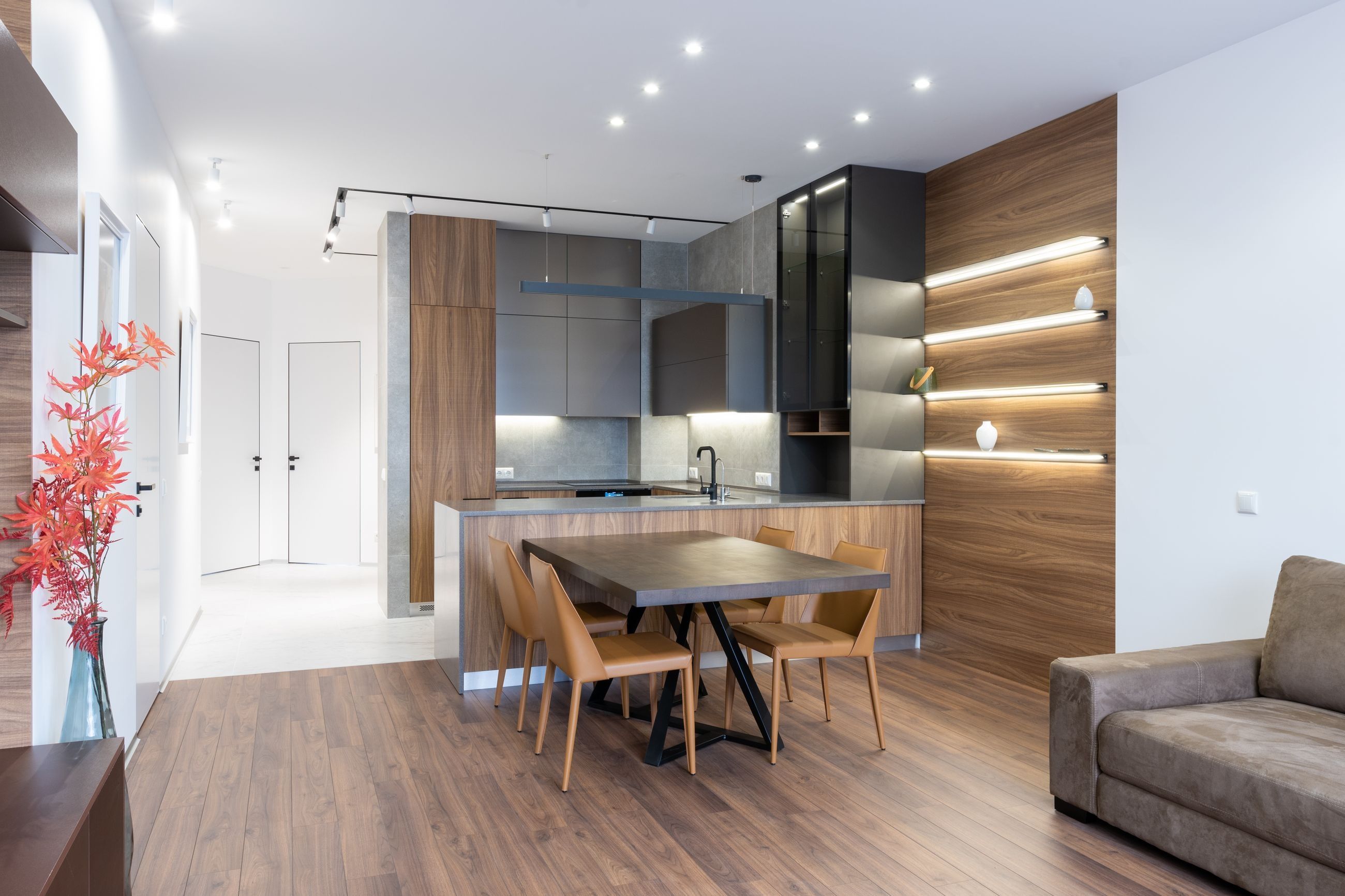 Piso reformado con cocina abierta en península, comedor y salón, revestimiento de madera con estantes iluminados y suelo laminado