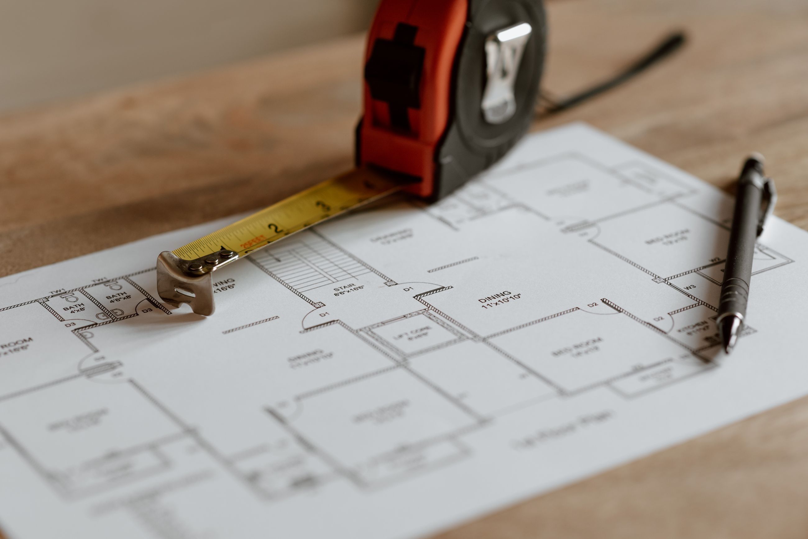 Plano de una vivienda sobre una mesa con un metro y herramientas de medición