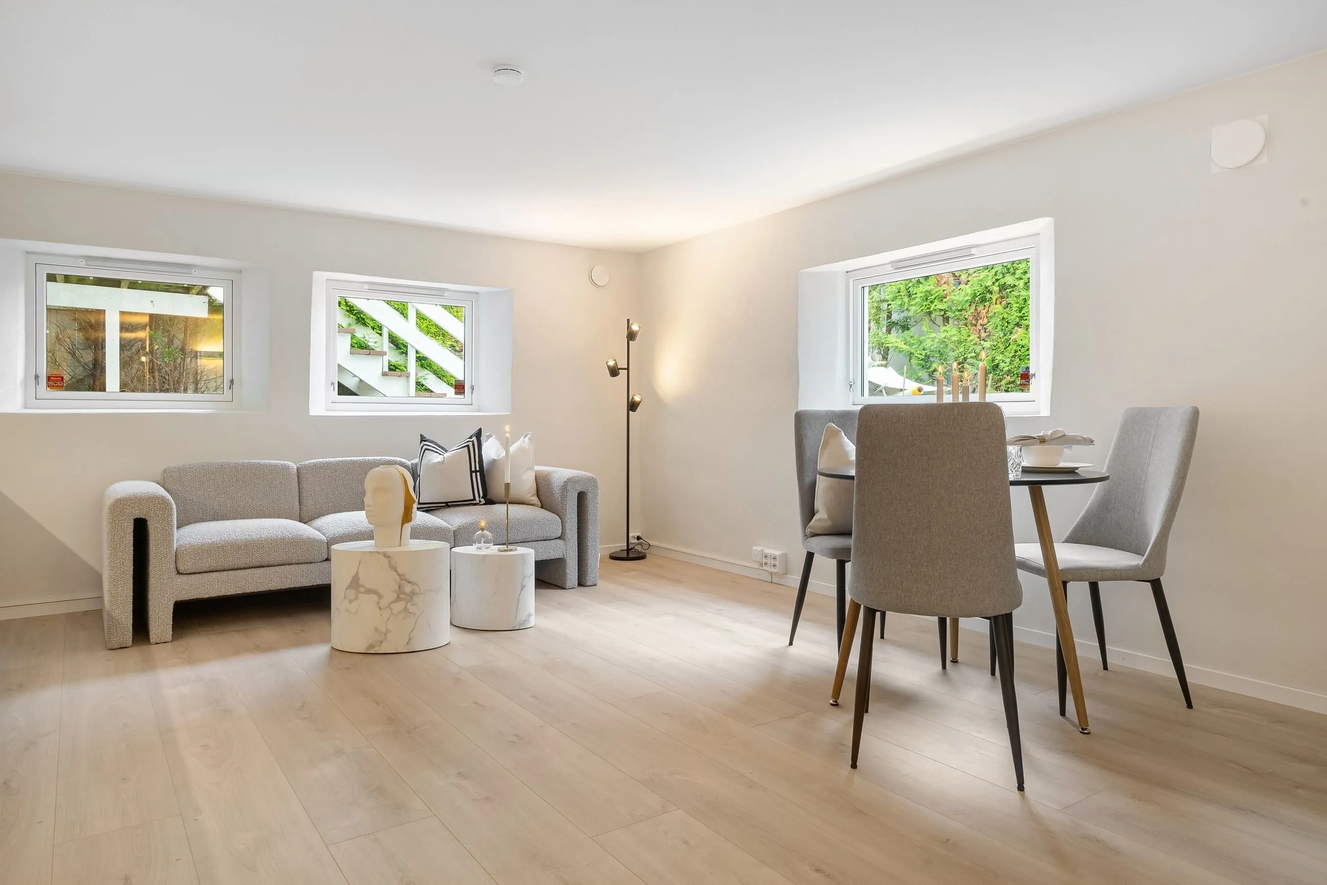 Salón luminoso con sofá gris, suelo de madera clara y comedor junto a la ventana